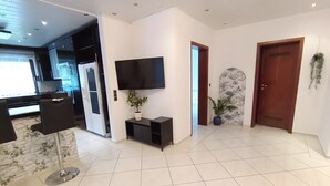A modern living room with a flat-screen TV, a potted plant, and a dining area with a black chair and table.