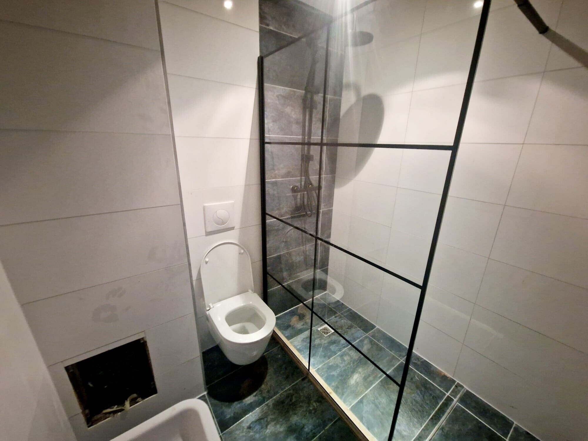 Un baño con inodoro, cabina de ducha y suelo de baldosas.