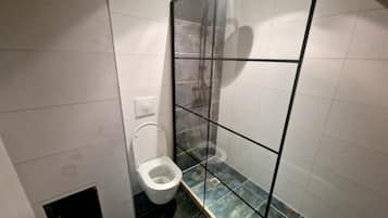Un baño con inodoro, cabina de ducha y suelo de baldosas.