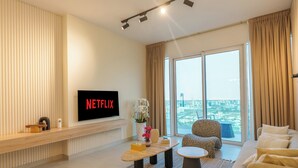 A modern living room with a flat-screen TV displaying 'NETFLIX,' a sofa, a coffee table, and a view of a cityscape through large windows. - Dubai Frame & Skyline View 2BR – 42nd Floor, Pool & Gym (Dubai)