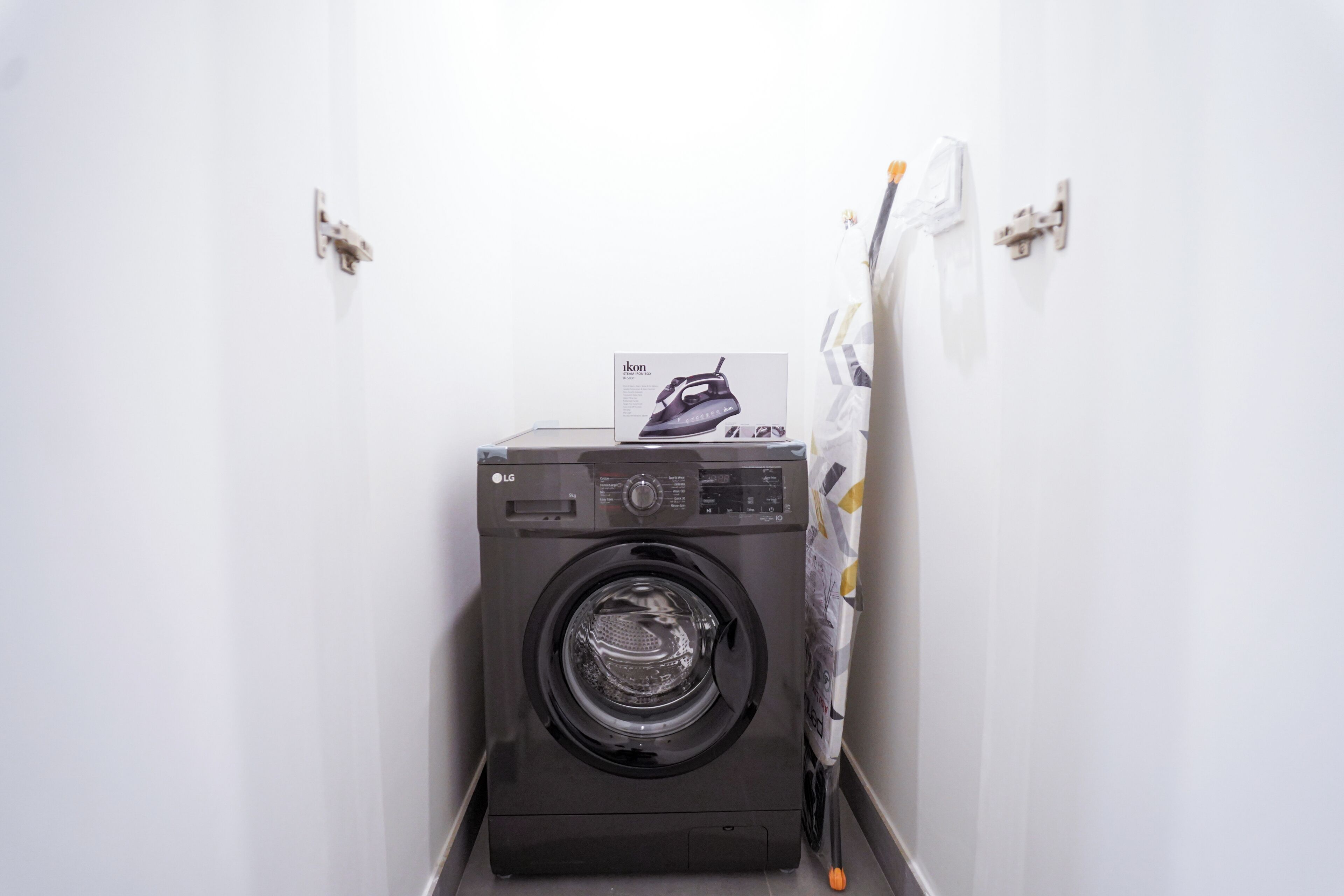 Une petite buanderie moderne, équipée d’un lave-linge à chargement frontal et d’un étendoir.
