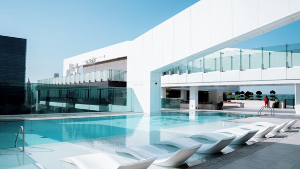A modern pool area with clear blue water, white lounge chairs, and a glass-enclosed upper level. - Dubai Frame & Skyline View 2BR – 42nd Floor, Pool & Gym (Dubai)