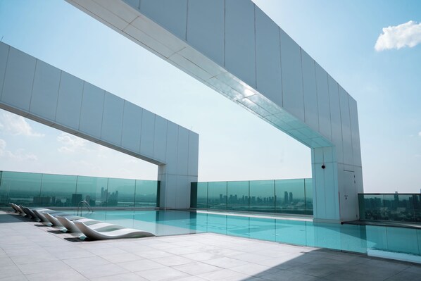 A modern rooftop pool with clear glass walls, a city skyline view, and a minimalist architectural design.