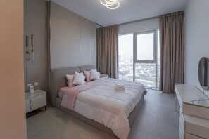 A modern bedroom with a large bed, a bedside table, a dresser, and a view of the city through large windows.