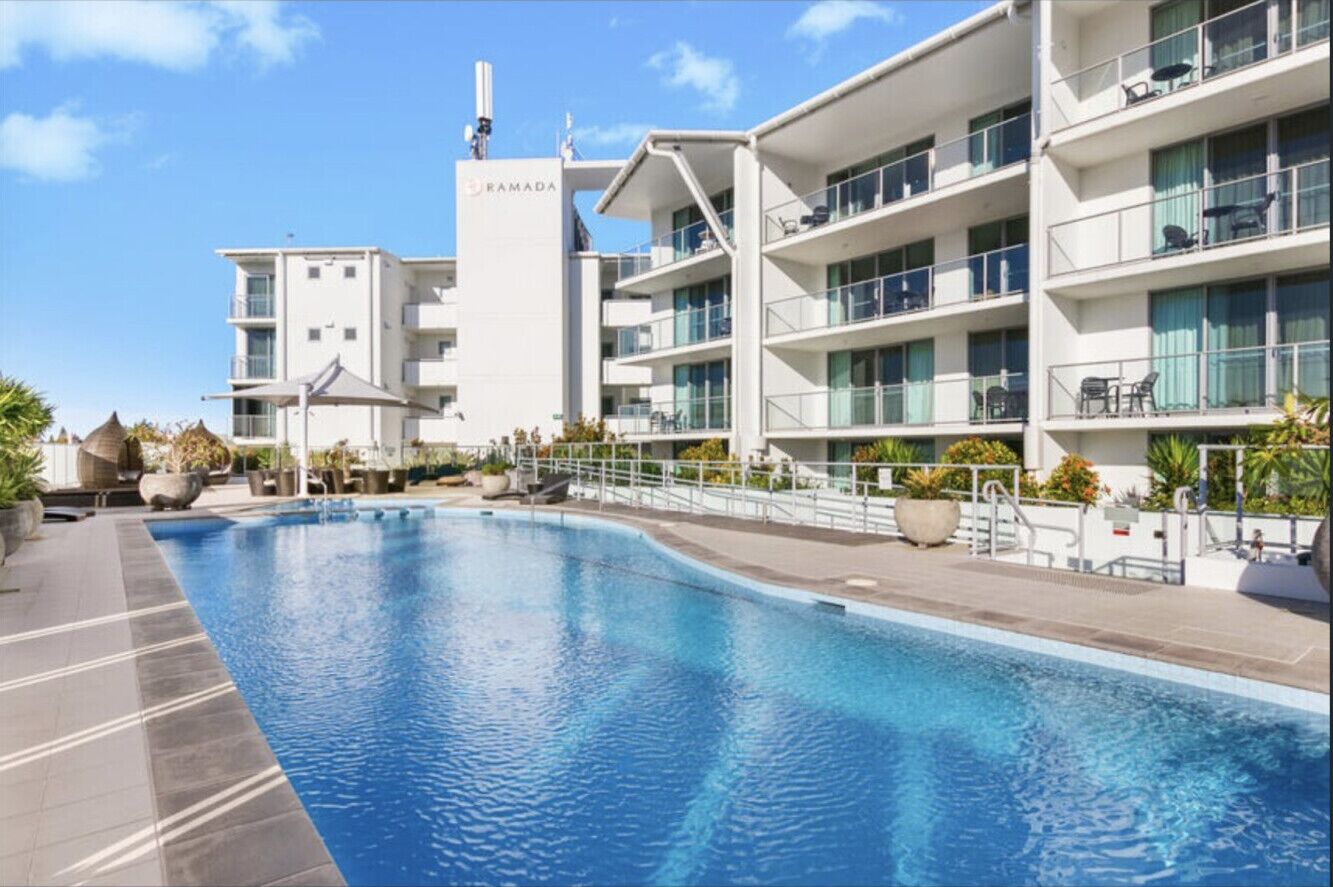 Ein modernes Hotel mit Schwimmbad, mehreren Balkonen und blauem Himmel.