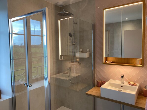 Une salle de bain moderne avec une douche à parois de verre, un grand miroir et un lavabo agrémenté d’articles de toilette.