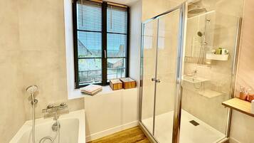 Ein modernes Badezimmer mit einer gläsernen Duschkabine, einer Badewanne und einem Fenster mit Jalousien.