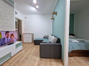 Una camera moderna con TV a schermo piatto, un mobiletto in legno, un divano grigio e un letto con coperta blu.