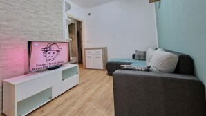 Ein modernes Wohnzimmer mit Flachbildfernseher auf einer weißen Unterhaltungsanlage, einem grauen Sofa und Holzboden.