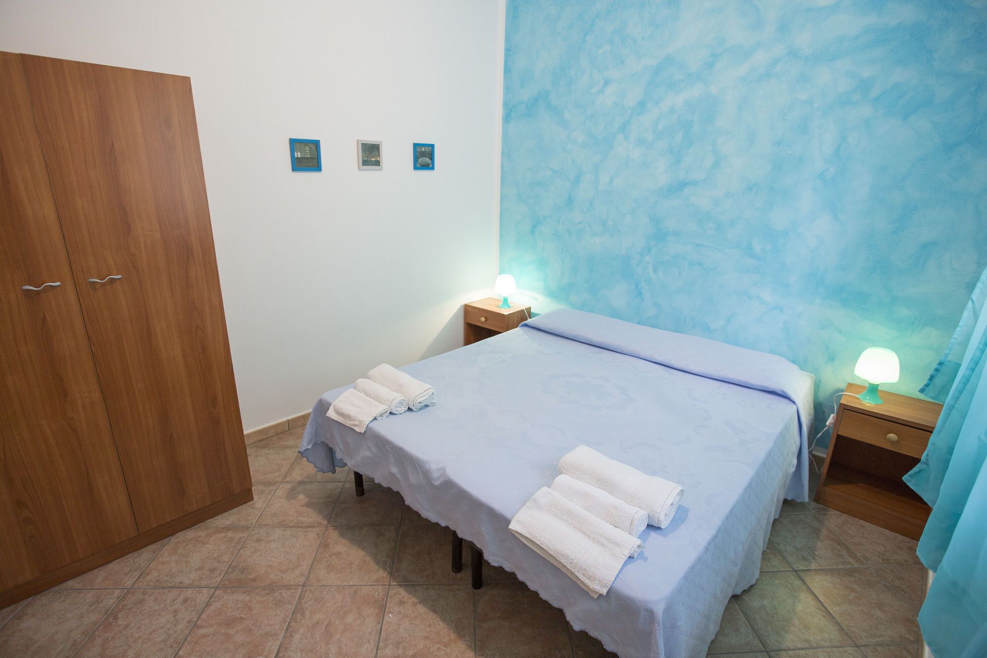 Un dormitorio con cama, dos mesitas de noche con lámparas, un armario de madera y una pared azul decorativa.