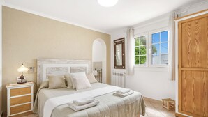 A bedroom with a bed, bedside table, lamp, mirror, window, and wardrobe. - Private villa with barbecue, ping pong, swimming pool and garden. 7 min from the beach! (Cala en Porter)