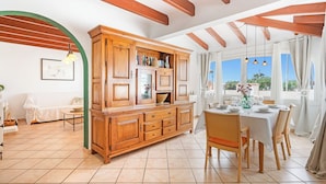 A dining area with a wooden cabinet, a dining table set for six, and a view of the outdoors through large windows. - Private villa with barbecue, ping pong, swimming pool and garden. 7 min from the beach! (Cala en Porter)