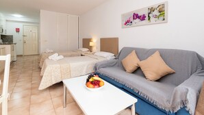 A hotel room with two beds, a sofa, a dining table with fruit, and a painting on the wall. - Central Studio Apartment. Communal Heated Pool (CN)