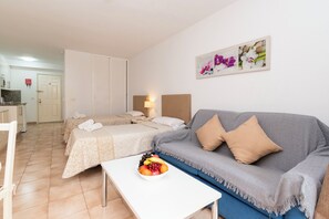 A hotel room with two beds, a sofa, a dining table with fruit, and a painting on the wall. - Central Studio Apartment. Communal Heated Pool (CN)