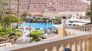 A hotel with a pool area, surrounded by palm trees and a view of a densely packed residential area with terraced buildings. - Central Studio Apartment. Communal Heated Pool (CN)