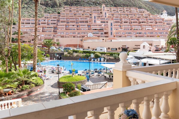A hotel with a pool area, surrounded by palm trees and a view of a densely packed residential area with terraced buildings. - Central Studio Apartment. Communal Heated Pool (CN)