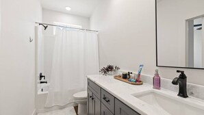 Ein modernes Badezimmer mit einer weißen Duschvorhang, einer weißen Toilette, einem Waschtisch mit Marmorplatte und einem schwarzen Wasserhahn.