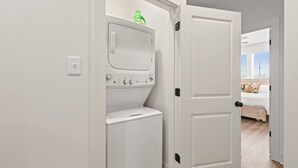 Ein Waschbereich mit Waschmaschine und Trockner, eine Tür zu einem Schlafzimmer mit Bett und Fenster.
