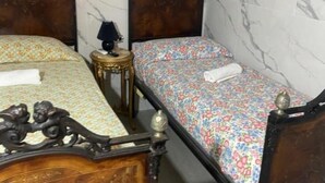 Een kamer met twee houten bedden, elk voorzien van een bloemenbedekking en een klein nachtkastje met een lamp.