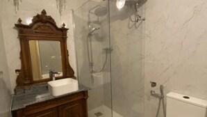 Een badkamer met een houten wastafelmeubel, een witte wastafel, een grote spiegel en een douchecabine met glazen wanden.