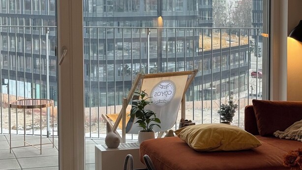 A modern living room with a large window, a sofa, a small table, and a potted plant.