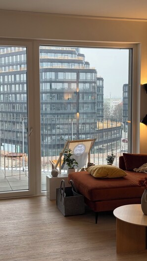 A modern living room with a large window, a sofa, a small table, and a potted plant. - Maison Ébène, warm, premium, and attractive for couples & business travelers. (Prague)
