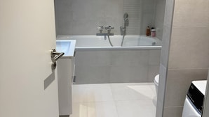 A modern bathroom with a bathtub, toilet, and a washing machine.