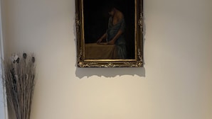 A room with a dark wooden bench, a patterned rug, a framed painting, and a tall vase with dried plants.