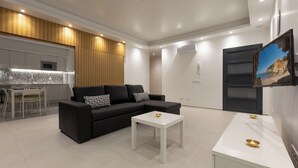 Ein modernes Wohnzimmer mit einer schwarzen Couch, einem weißen Couchtisch und einer Küchenzeile im Hintergrund.