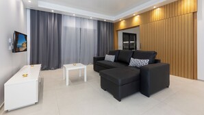 Ein modernes Wohnzimmer mit einem Ecksofa, einem kleinen weißen Tisch und einem an der Wand montierten Fernseher.