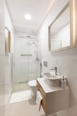 Een moderne badkamer met een douche met glazen wand, een wit wastafelmeubel en een grote spiegel.
