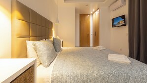 Ein modernes Hotelzimmer mit einem großen Bett, einem Kopfteil, einem Nachttisch, einer Lampe, einem Bild an der Wand und einer Klimaanlage.