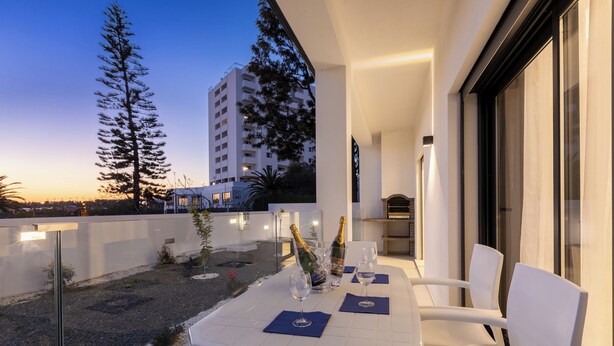 Eine Dachterrasse mit Tisch für zwei Personen, Gartenmöbeln und Blick auf eine Stadtlandschaft im Abenddämmerung.
