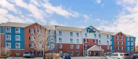 A multi-story hotel with a mix of red and blue exterior walls, a parking lot, and a clear sky.