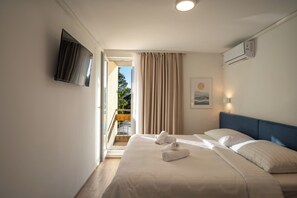 Ein Hotelzimmer mit Bett, Flachbildfernseher an der Wand, einem Fenster mit Vorhängen und einer Klimaanlage.