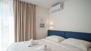 A hotel room with a bed, two pillows, a headboard, an air conditioning unit, a window with curtains, and a wall-mounted light. - Alemaris Resort (Baška Voda)