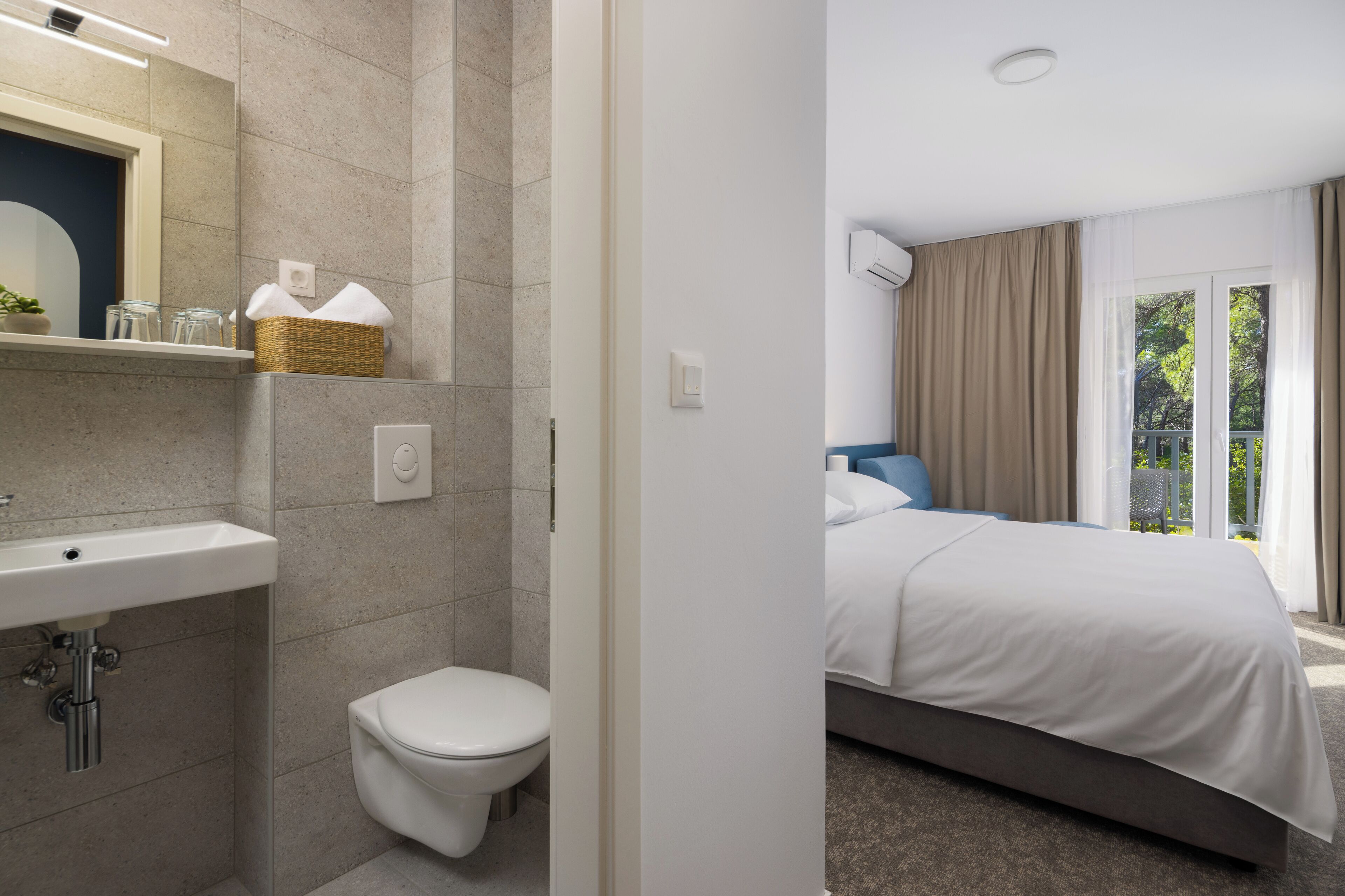 Un bagno moderno con lavandino, WC e doccia. La stanza ha un'ampia finestra con tende e vista sul verde.