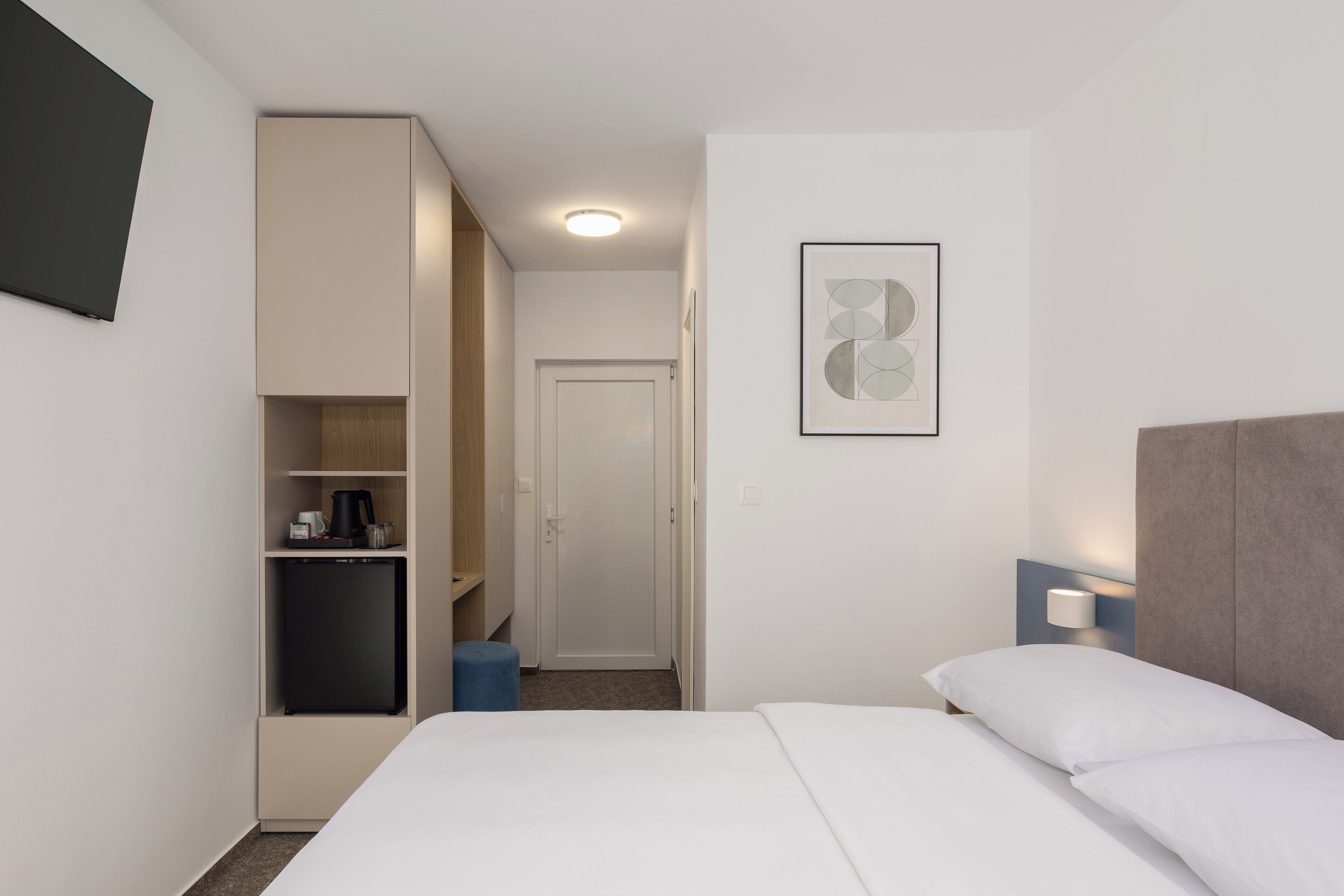 A hotel room with a bed, a wardrobe, a small kitchenette, and a door leading to another room.