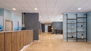 A reception area with a wooden counter, a blue wall with a logo, a grey wall with shelves, and a tiled floor. - Alemaris Resort (Baška Voda)
