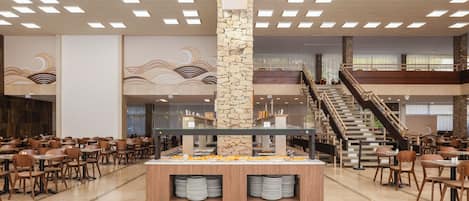 A buffet area with a central serving counter, multiple dining tables, and a staircase leading to an upper level.