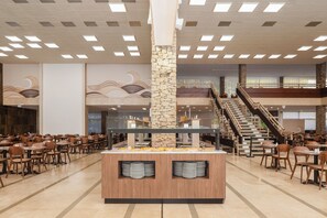 Ein Bereich mit Buffet, einer zentralen Anrichte, mehreren Esstischen und einer Treppe, die in eine obere Ebene führt.