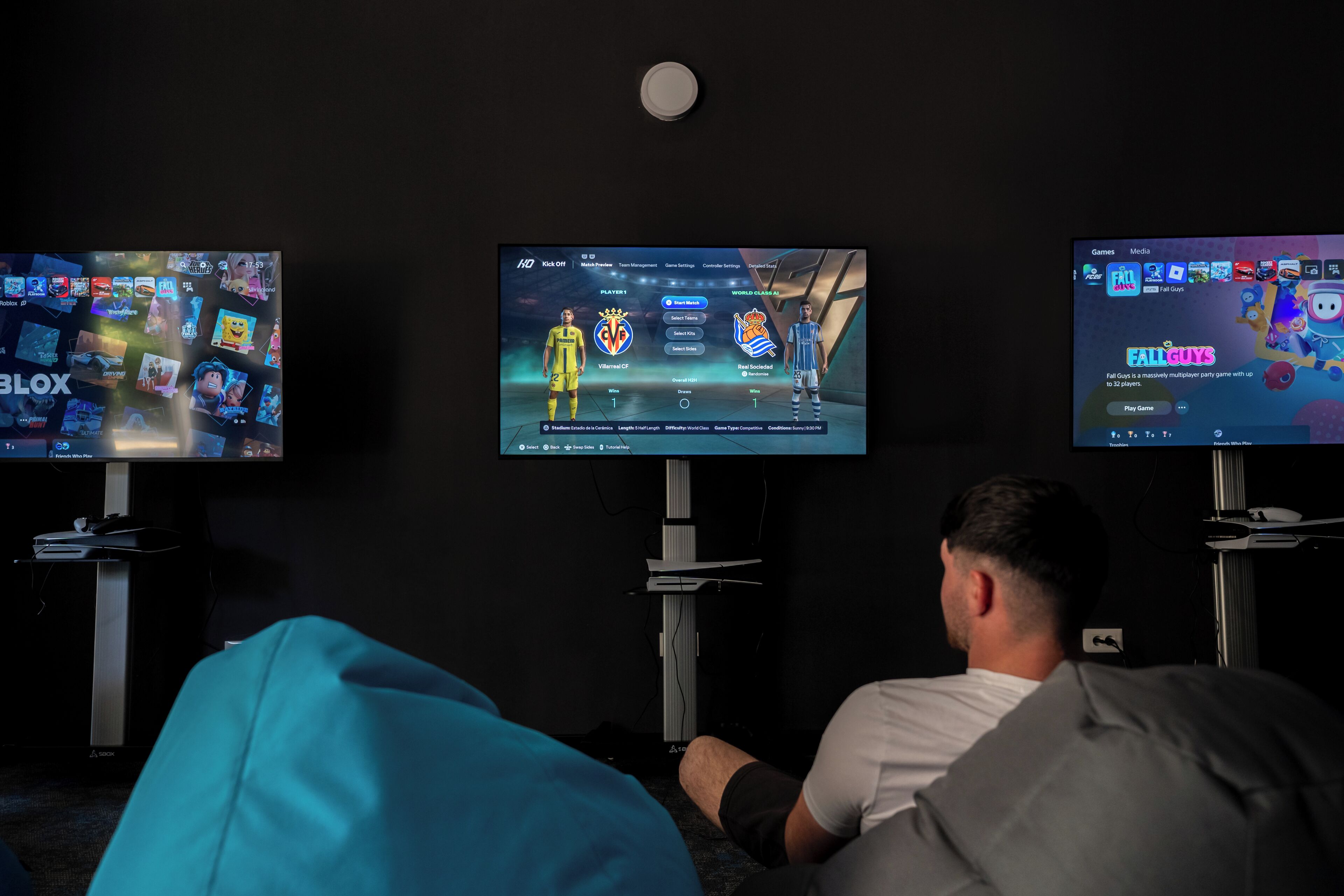 Trois écrans affichant des jeux vidéo, avec une personne assise devant.