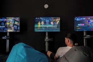 Three screens displaying video games, with a person seated in front of them. - Alemaris Resort (Baška Voda)