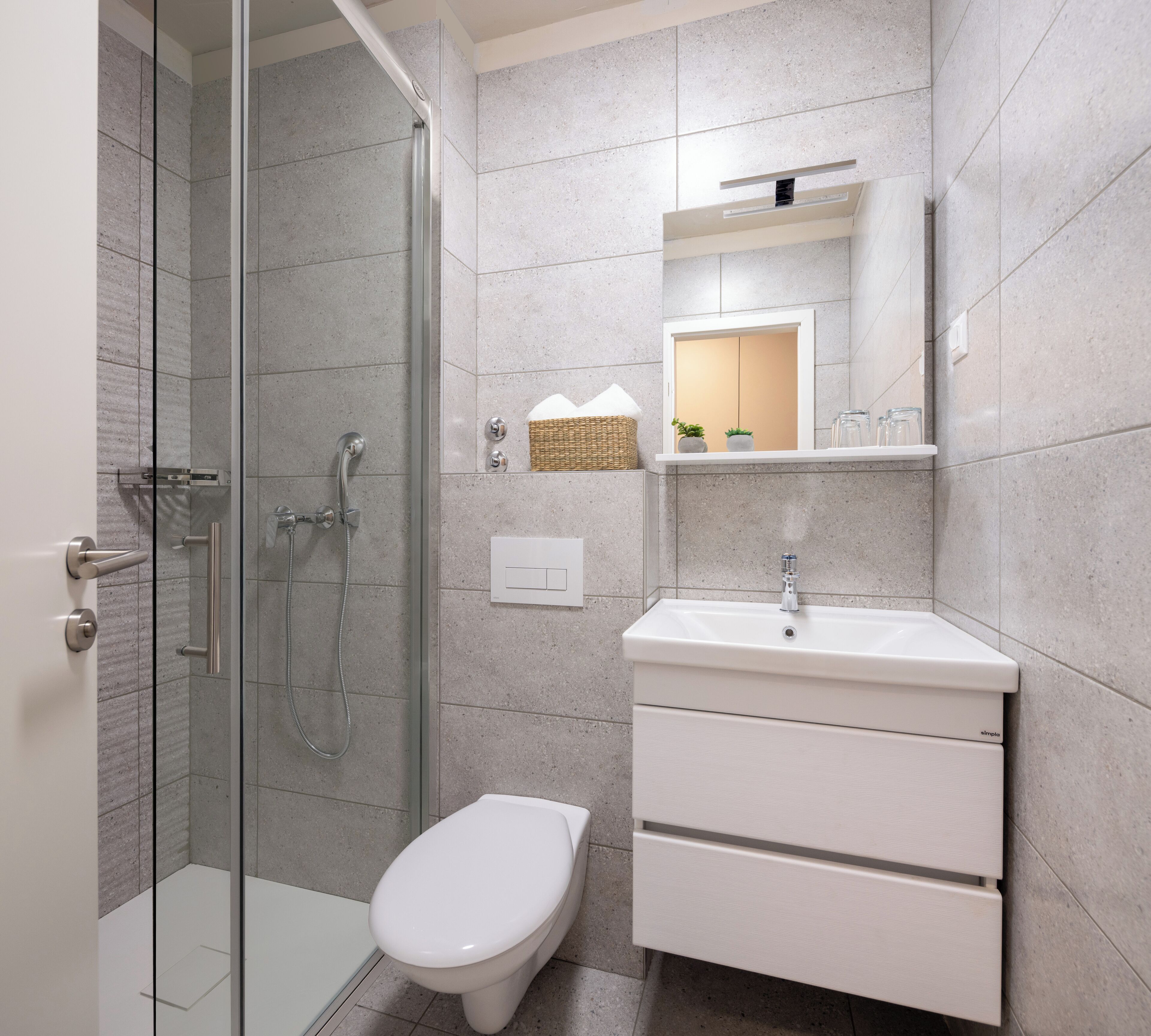 A modern bathroom with a glass-enclosed shower, a white toilet, and a white sink with a mirror above it.