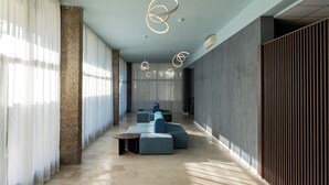 A modern interior with a long corridor, seating area, and a large window with sheer curtains.