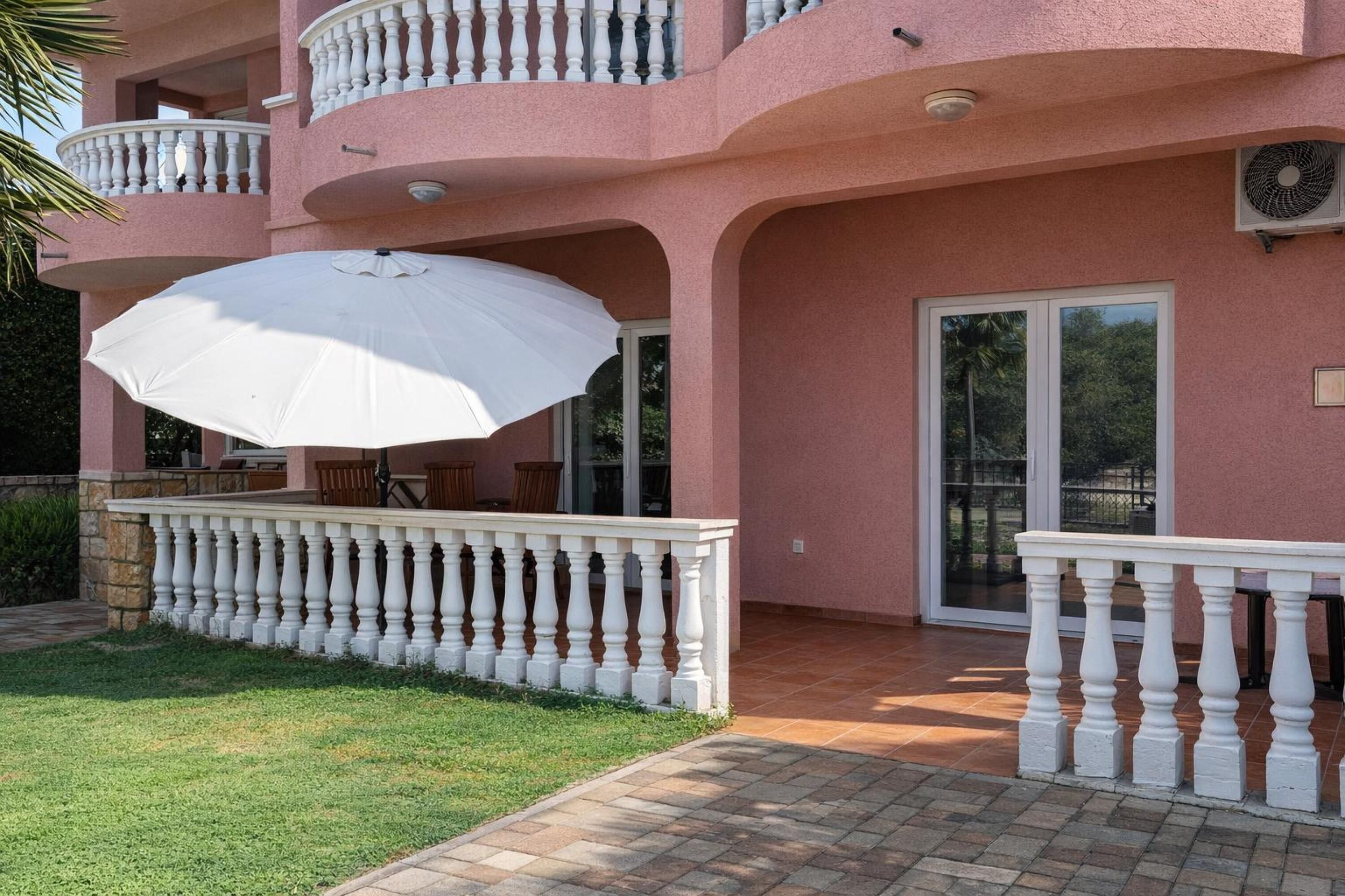 Een roze gebouw met een balkon, een witte parasol en een terras.