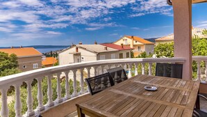 Ein Balkon mit einem Holztisch und Stühlen, einem weißen Geländer und Blick auf Häuser sowie ein Gewässer.
