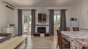 Ein modernes Wohnzimmer mit Sofa, Fernseher, Esstisch und Stühlen.