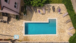 Ein Pool auf dem Dach mit Steinfliesen, umgeben von Liegestühlen und einer Steinmauer.