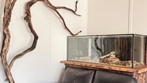 A room with a black leather sofa, a glass fish tank on a wooden stand, and a large branch decoration on the wall.
